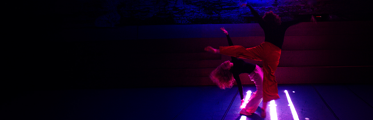 Zwei Menschen tanzen in einem dunklen Raum. 