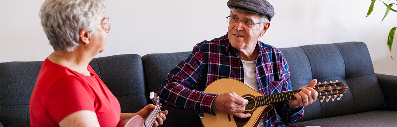 Seniorin und Senior spielen auf einer Ukulele