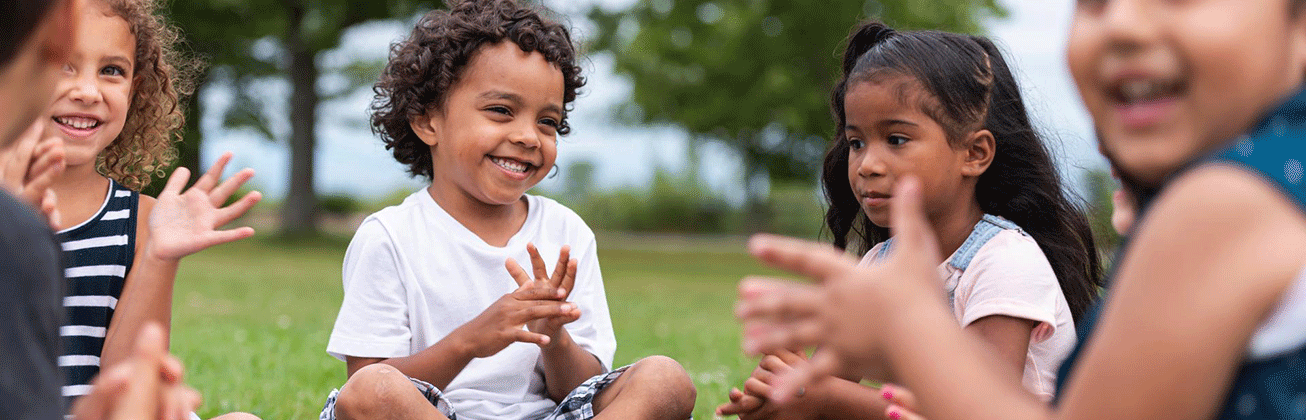 4 Kinder sitzen im Gras und klatschen