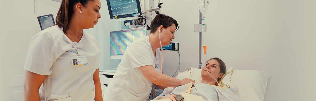 Pflegefachpersonen untersuchen eine Patientin im Spitalbett, umgeben von medizinischen Geräten.