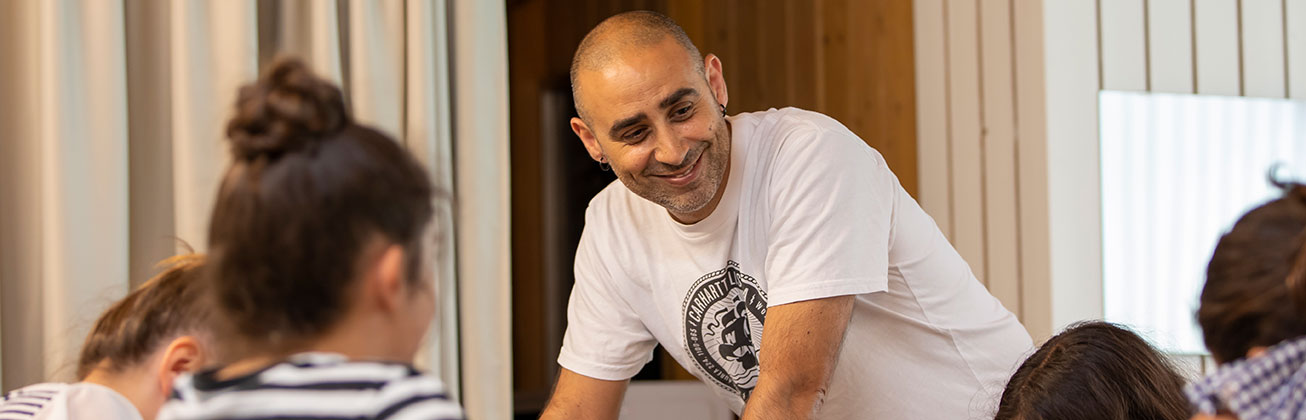 Ein lächelnder Mann der sich auf einem Tisch abstützt und Kinder betreut