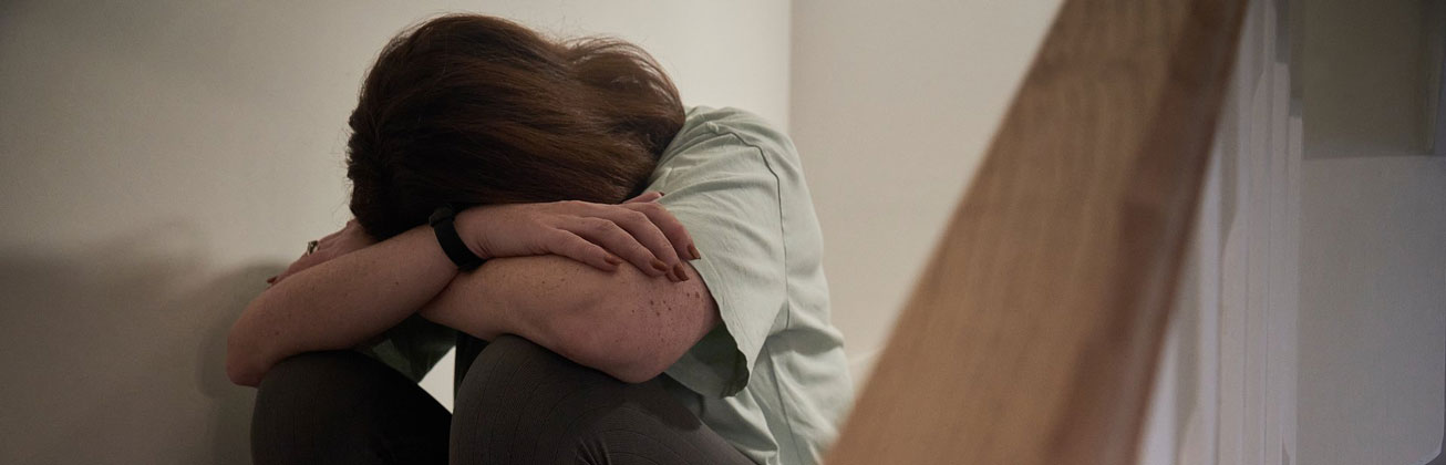 Frau sitzt auf Treppe und verdeckt Gesicht