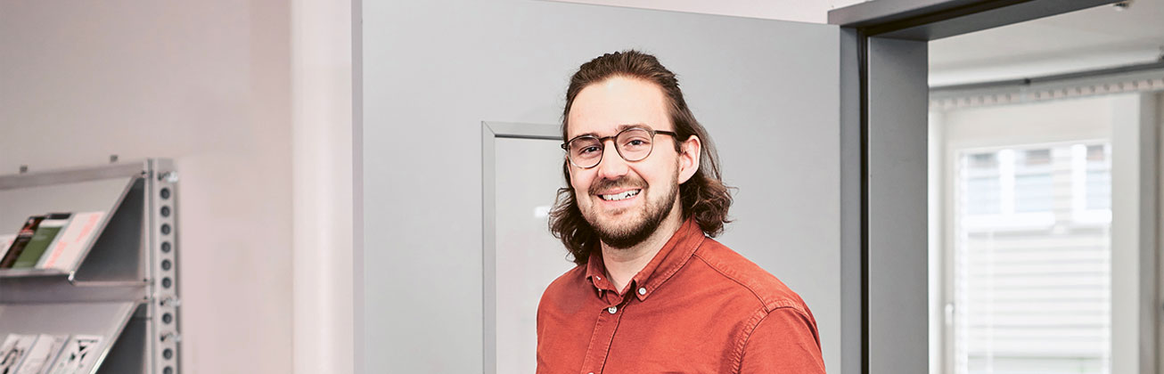 Ein lächelnder Master-Absolvent vor weissem Hintergrund