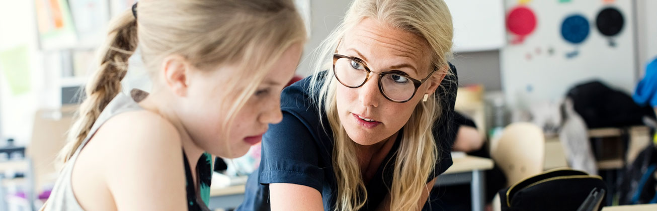Eine Frau erklärt einem Mädchen etwas in einem Klassenzimmer