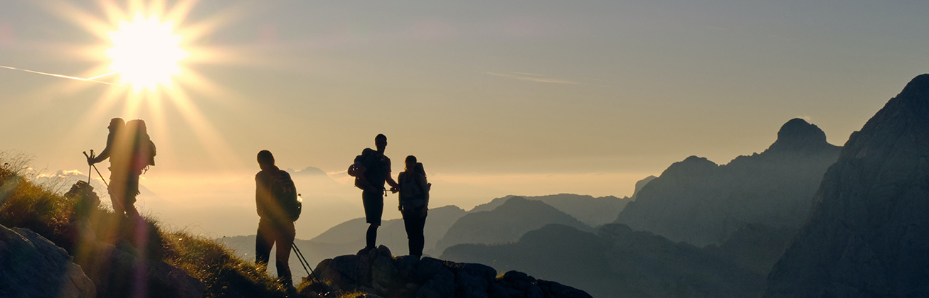 Foto zeigt eine Gruppe von wandernden Menschen, die bei Sonnenaufgang einen Berg hochsteigen.