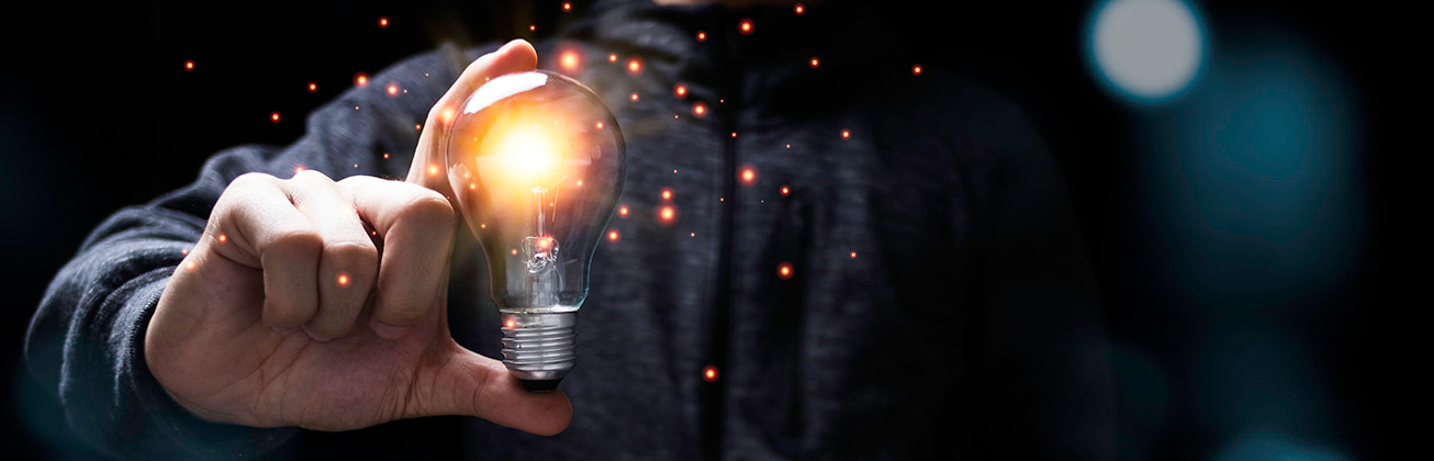 Foto zeigt einen Mann, der eine leuchtende Glühbirne zwischen den Fingern hält.