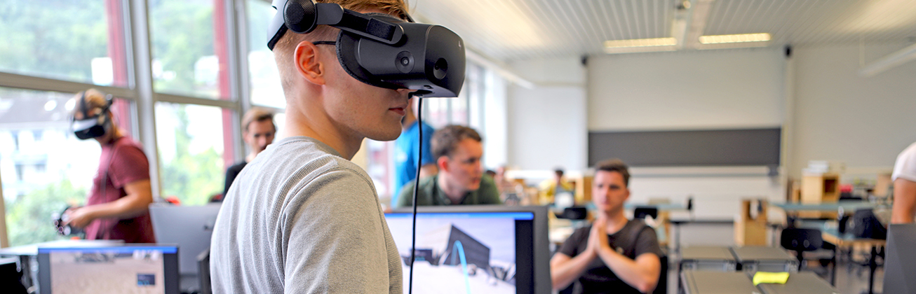 Ein Student trägt eine VR-Brille und im Hintergrund sind weitere Technik-Studierende zu sehen