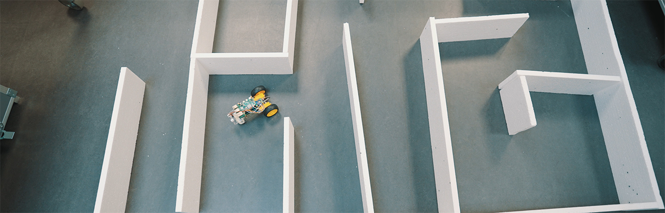 Kleiner mobiler Roboter fährt durch ein Parcours-Labyrinth aus weißen Wänden – praxisnahe Robotik-Experimente und flexible Lernumgebung