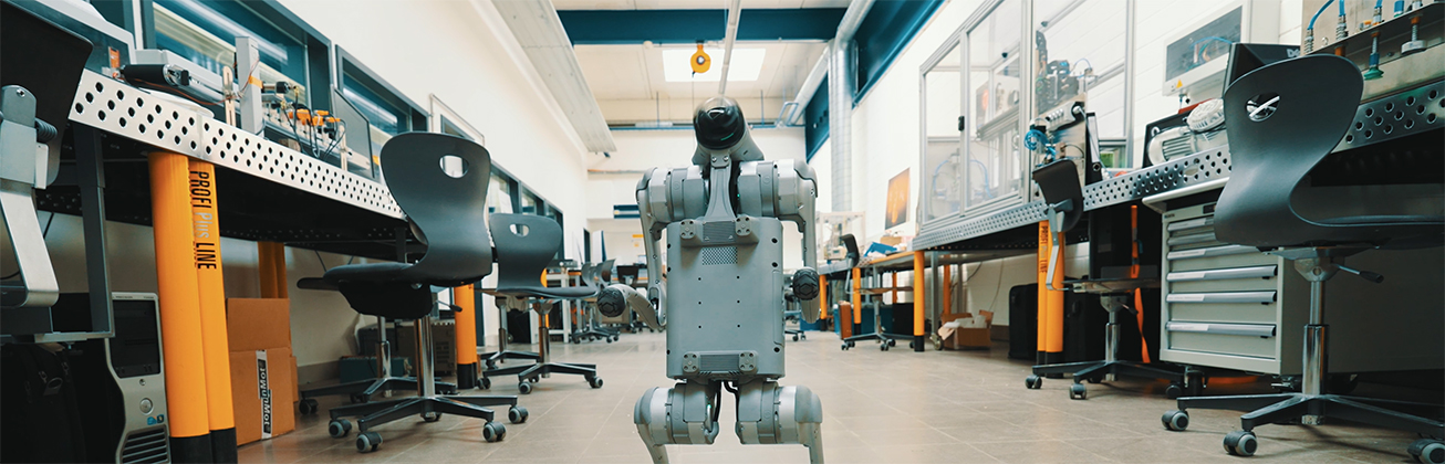 Kleiner hundeartiger Roboter steht in einem modernen Robotiklabor mit Werkbänken, Computern und Arbeitsstühlen – Forschung und Entwicklung in der Robotik