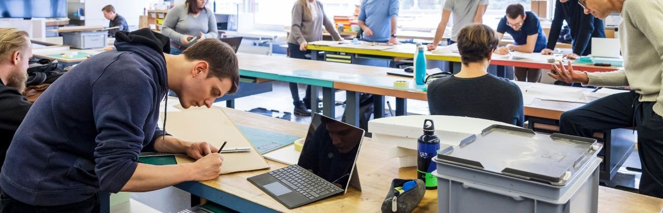 Studierende arbeiten an Entwürfen und Prototypen in einer offenen Werkstattumgebung