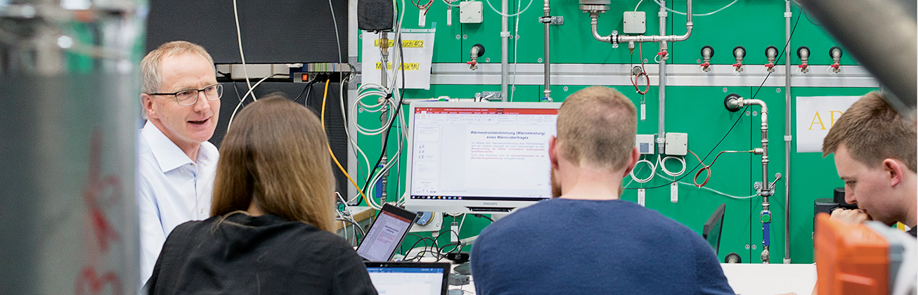 Vier Personen in einem technischen Arbeitsraum sitzen an Laptops und diskutieren