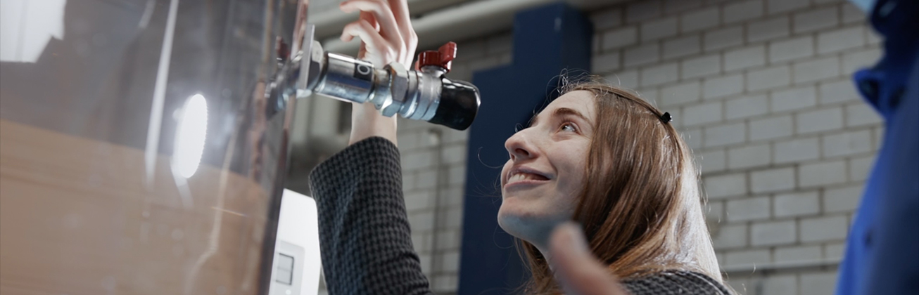 Die Absolventin Jessica Stoller prüft lächelnd etwas an einem Wassertank