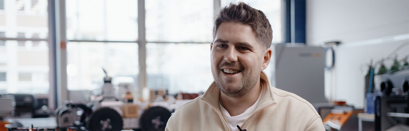 Portrait des Absolventen Mattia Heuberger, der glücklich in die Kamera schaut und sich in industriellen Büro-Räumlichkeiten befindet