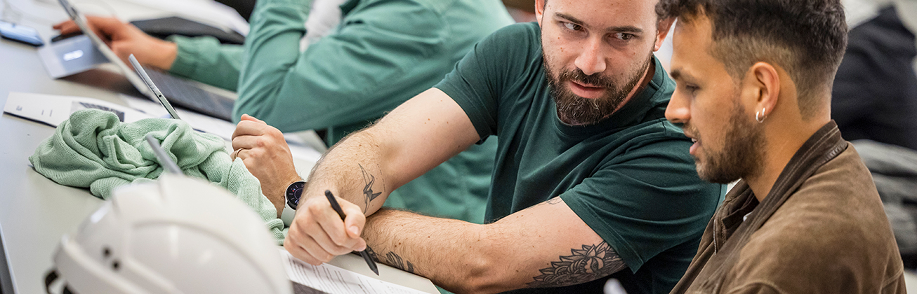 zwei junge maenner im unterricht mit helm auf tisch