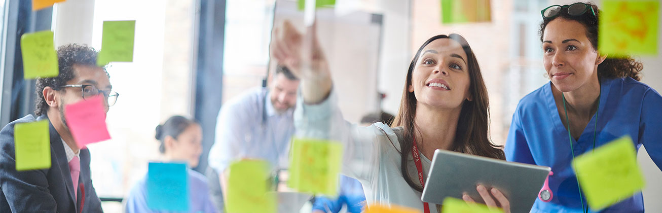 Studierende diskutieren Ideen an einer Glaswand mit handgeschriebenen Notizen.