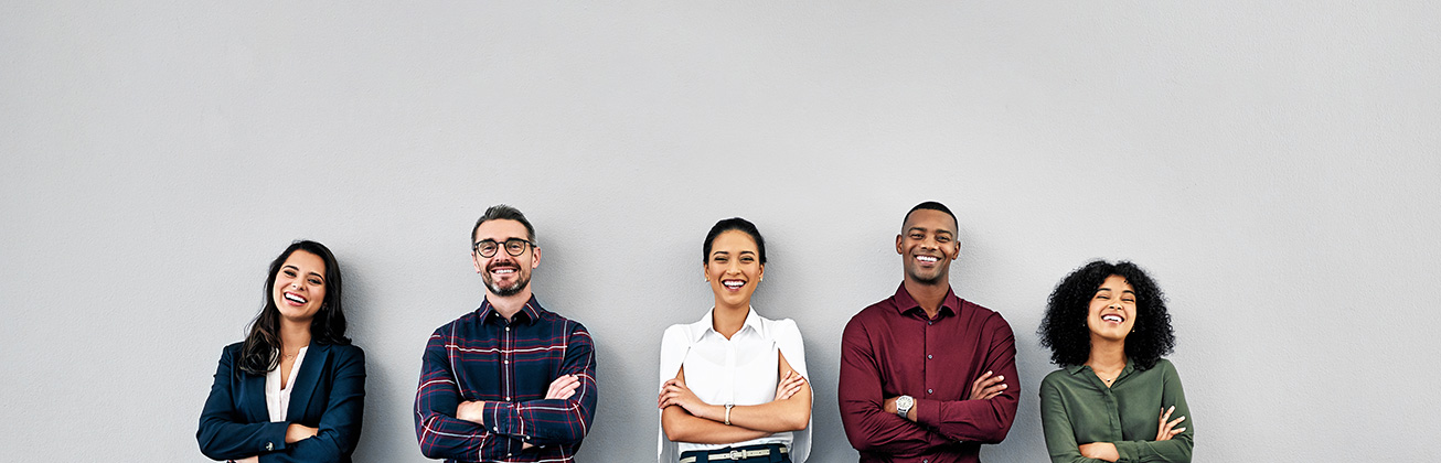 Fuenf laechelnde Personen unterschiedlicher Herkunft, die vor einem neutralen grauen Hintergrund stehen