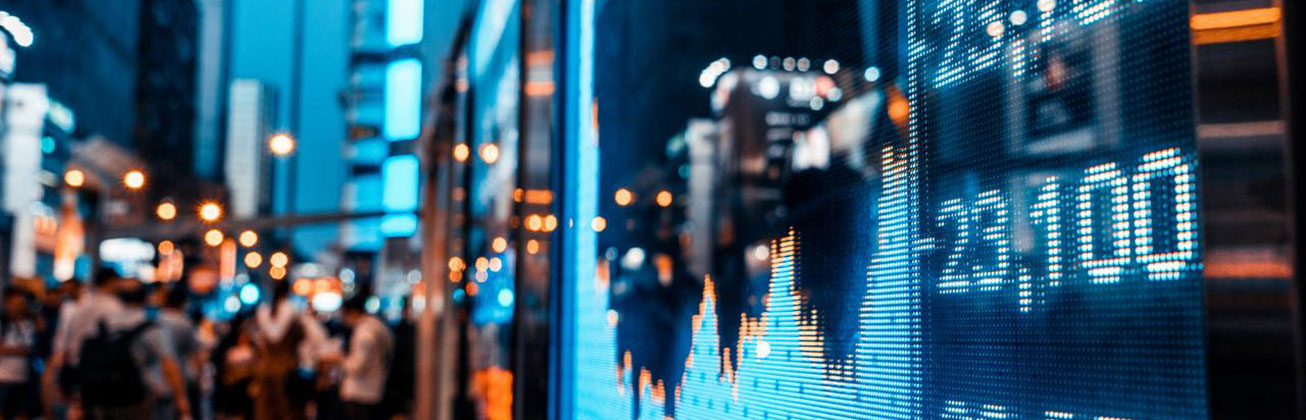 Börsenkurse auf einer digitalen Wand, im Hintergrund Menschen