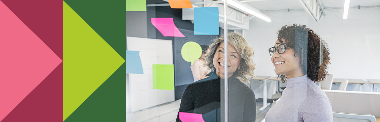 Zwei Personen stehen vor einer Glaswand mit bunten Post-its und lächeln – Sinnbild für kreative Ideenfindung, nutzerzentrierte Prozesse und die Gestaltung digitaler Kundenerlebnisse.