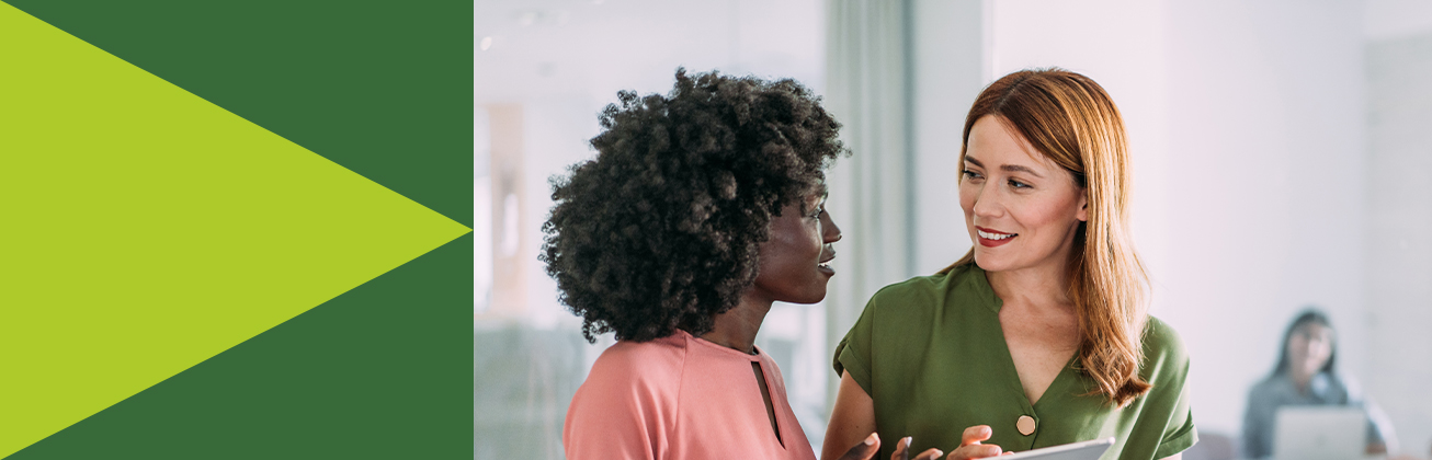 Zwei Personen stehen im Gespräch in einer modernen Umgebung, eine hält ein Tablet – Symbolbild für digitale Marketingkommunikation, strategische Abstimmung und kollaborative Zusammenarbeit.
