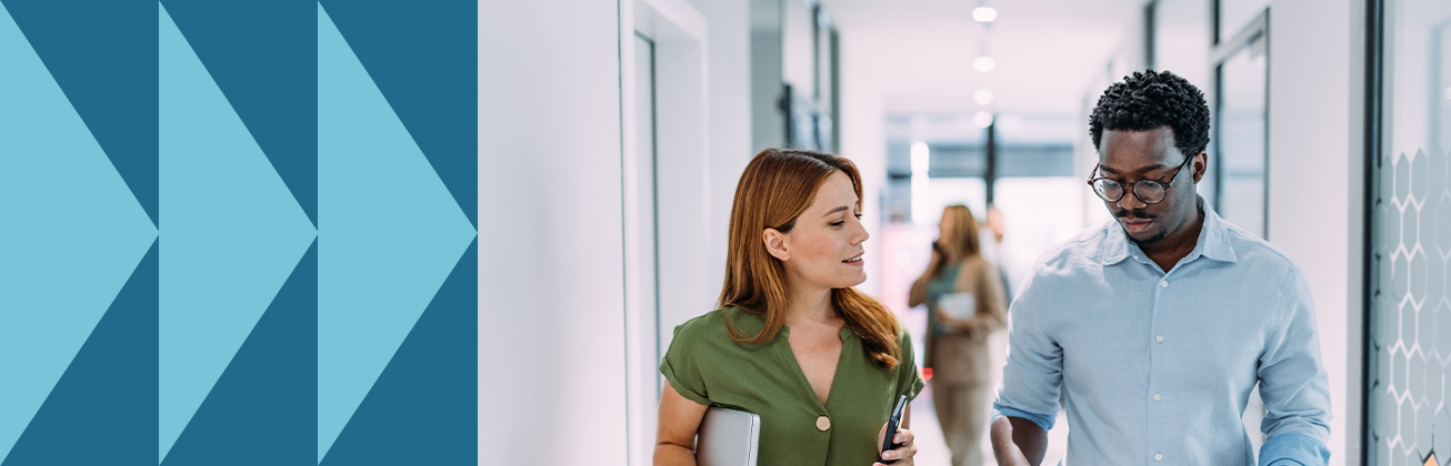 Eine Frau mit Laptop und ein Mann mit Tablet gehen durch ein modernes Büro und sprechen miteinander – Symbolbild für strategische Content-Planung, mobile Zusammenarbeit und zielorientierte Kommunikation.