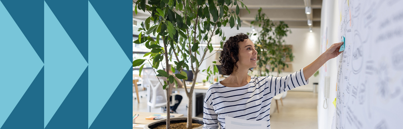 Eine Fachperson platziert ein Post-it auf einer Wand voller Skizzen und hält dabei Unterlagen – Symbolbild für datenbasierte Entscheidungsprozesse, visuelle Planung und strategische Analyse im Arbeitsalltag.