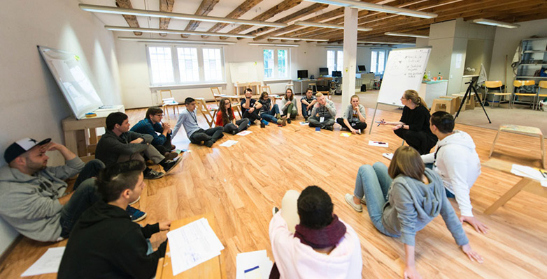 Gruppe von Studierenden sitzt im Kreis auf dem Boden