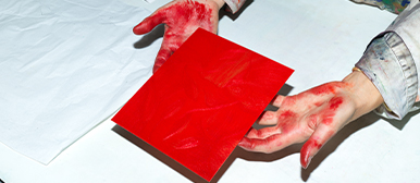 HSLU Design Film Kunst – Studierende arbeiten mit roter Farbe an einer Druckplatte im Gestaltungsunterricht.