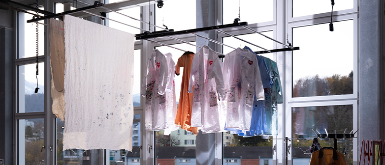 Kreativprozess sichtbar – bemalte Kittel hängen im Atelier der HSLU Design Film Kunst zum Trocknen.