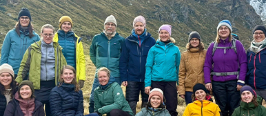  Gruppe von Menschen in Outdoor-Kleidung posiert gemeinsam in einer Berglandschaft vor felsigem Hintergrund.
