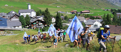 Eine Wandergruppe wandern mit Flaggen den Berg hoch. 