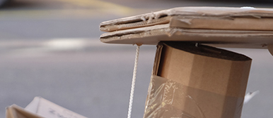     Gestapelte Karton- und Papiermaterialien werden mit Schnur zusammengehalten und zeigen ein improvisiertes Konstrukt im urbanen Raum.
