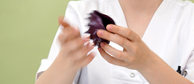     Person in weisser Arbeitskleidung hält ein violettes, organisch geformtes Objekt in den Händen und untersucht dessen Materialeigenschaften.
