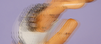     Bewegungsunschärfe einer Hand mit Holzobjekt vor violettem Hintergrund, die Dynamik und Interaktion mit dem Material sichtbar macht.
