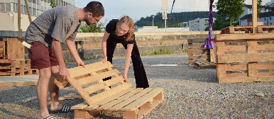 Eine Frau und ein Mann bauen aus zwei Holzpalletten eine Sitzmöglichkeit