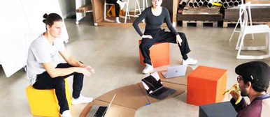 Studierende sitzen auf orangen und gelben Hockern und besprechen etwas