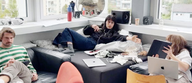 Drei Studierende arbeiten in einem Atelierzimmer an ihren Laptops und zwei interagieren miteinander