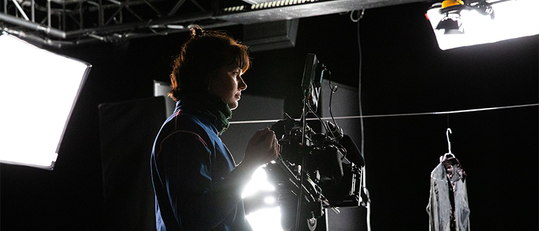 Ein Filmstudio mit grossen Lichtern und einer Frau, die eine Videokamera bedient. 