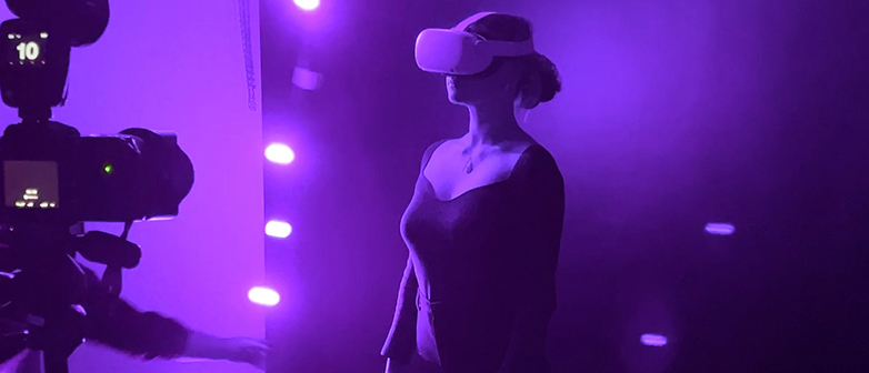 Person mit VR-Brille steht in violettem Licht, links eine Kamera im Vordergrund.