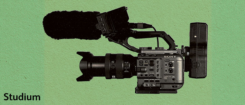 Eine schwarze Filmkamera mit Mikrofon auf einem grünen Hintergrund ausgelegt