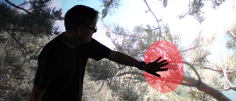 Image provided by Marcus Maeder - person standing in front of a screen and touching a red point in interacting with the installation.
