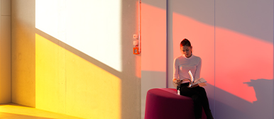 Licht und Raum im Studienalltag – Studierende liest im farbig beleuchteten Flur der HSLU Design Film Kunst.