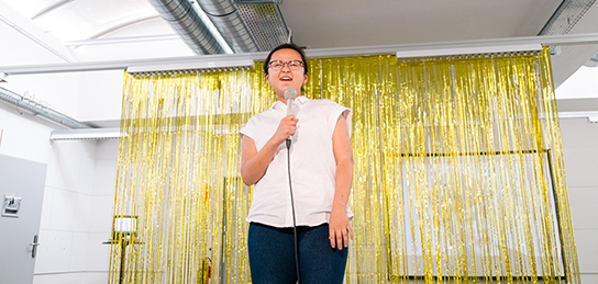 Junge Frau mit Mikrophon vor goldigem Vorhang