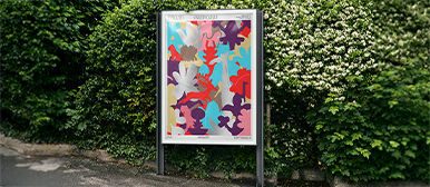 Plakat in Leuchtrahmen am Strassenrand – Sentitreff-Sommerplakat mit grafischem Pflanzenmotiv, ausgestellt im Strassenplakatkasten vor dichter Hecke.