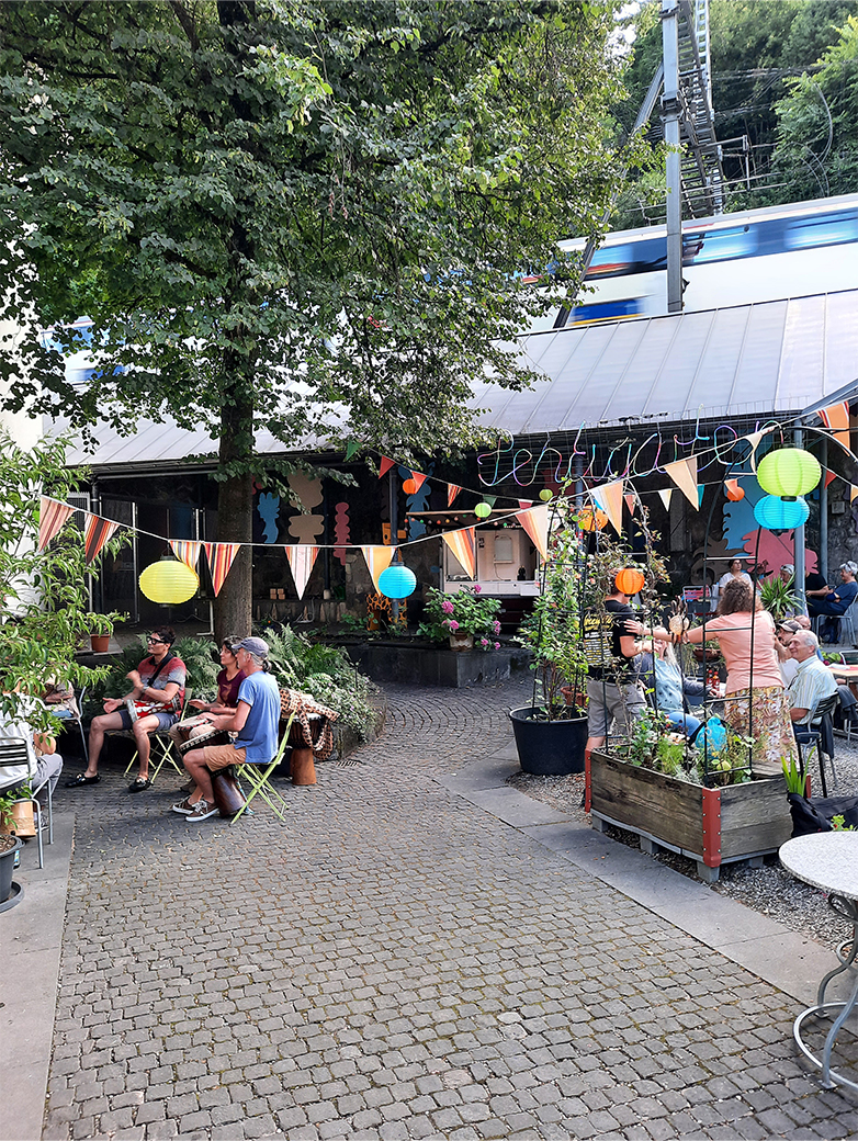 Bunt gestaltete Plakate und Drucksachen im öffentlichen Raum sowie Szenen eines lebendigen Quartiertreffs mit Menschen, Pflanzen und gemeinschaftlichen Aktivitäten im Aussenbereich.