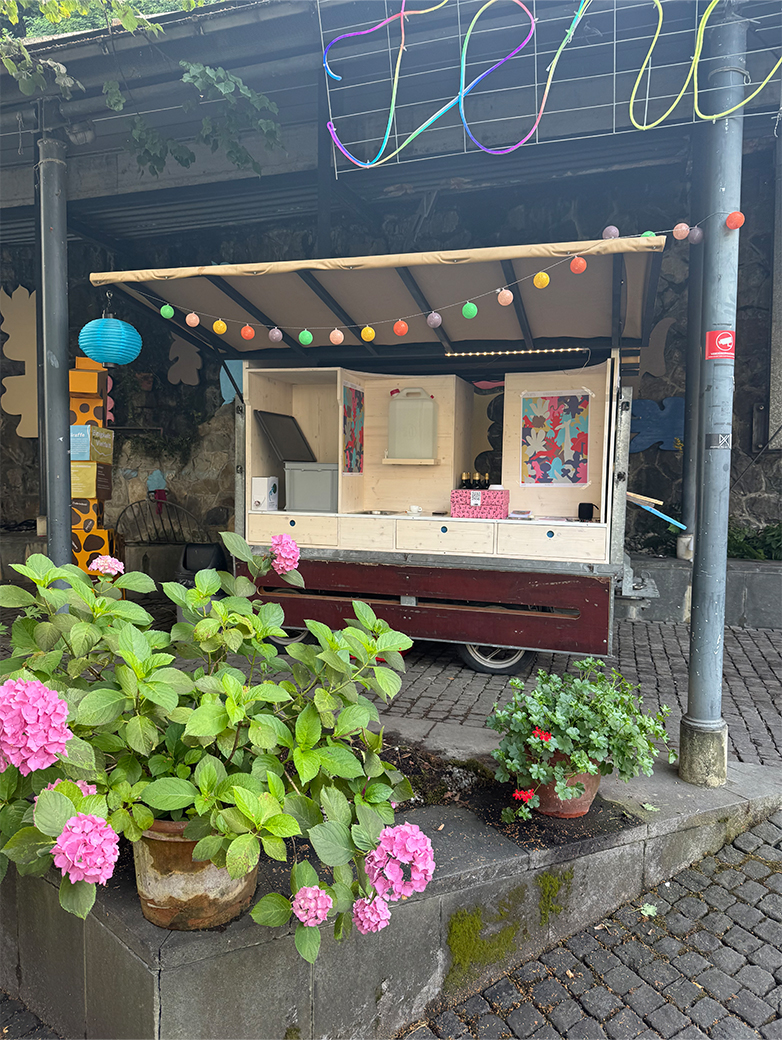 Bunt gestaltete Plakate und Drucksachen im öffentlichen Raum sowie Szenen eines lebendigen Quartiertreffs mit Menschen, Pflanzen und gemeinschaftlichen Aktivitäten im Aussenbereich.