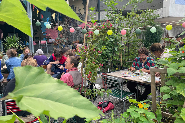 Bunt gestaltete Plakate und Drucksachen im öffentlichen Raum sowie Szenen eines lebendigen Quartiertreffs mit Menschen, Pflanzen und gemeinschaftlichen Aktivitäten im Aussenbereich.