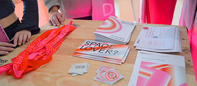 Blick auf einen Tisch mit pinken und orangenen Informationsmaterialien, Broschüren und Flyern, darunter ein auffälliger Schriftzug ‘SPACE LOVER?’ – Einblick in die Projektkommunikation von Nodo.