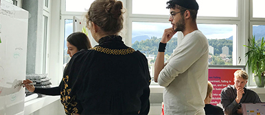 Eine Gruppe von Studierenden bespricht ein an der Wand verschiedene Designprozesse. 