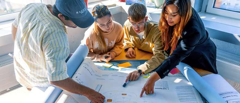 Eine Gruppe von Studierenden bespricht ein Designposter. 