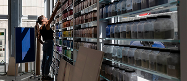 Eine Frau im Raum für Farben greift nach etwas im Regal. 